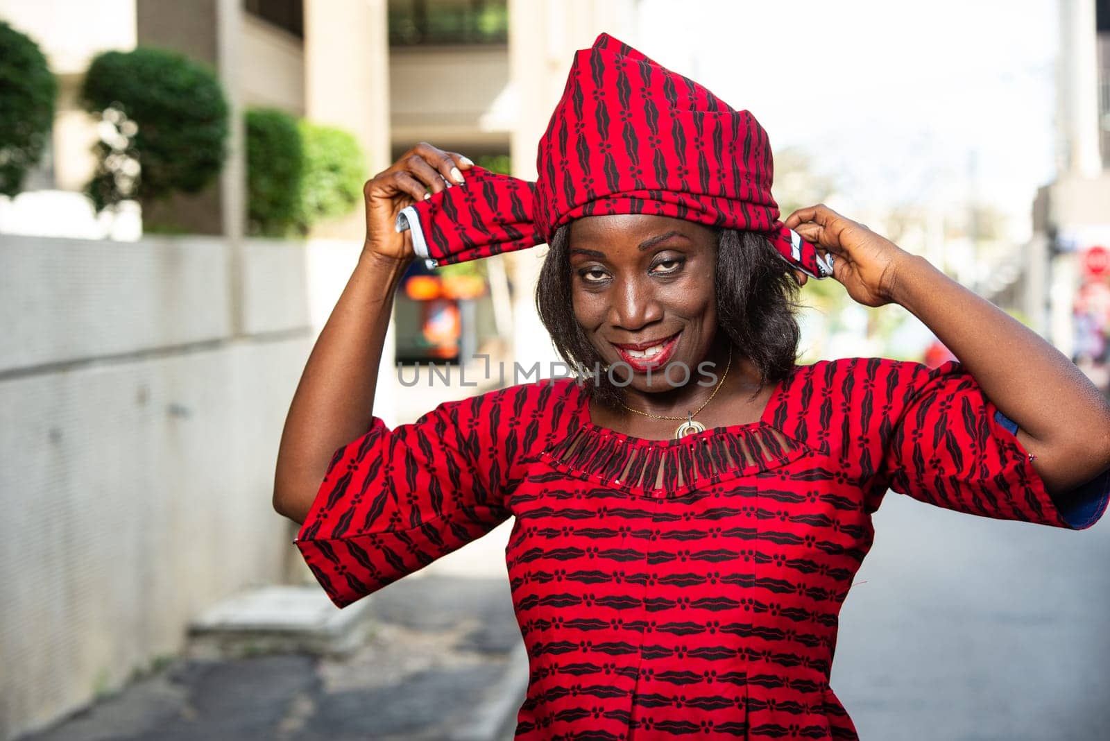 fashionable stylish african woman wearing a red loincloth straps a scarf on her head while smiling in the street in daylight