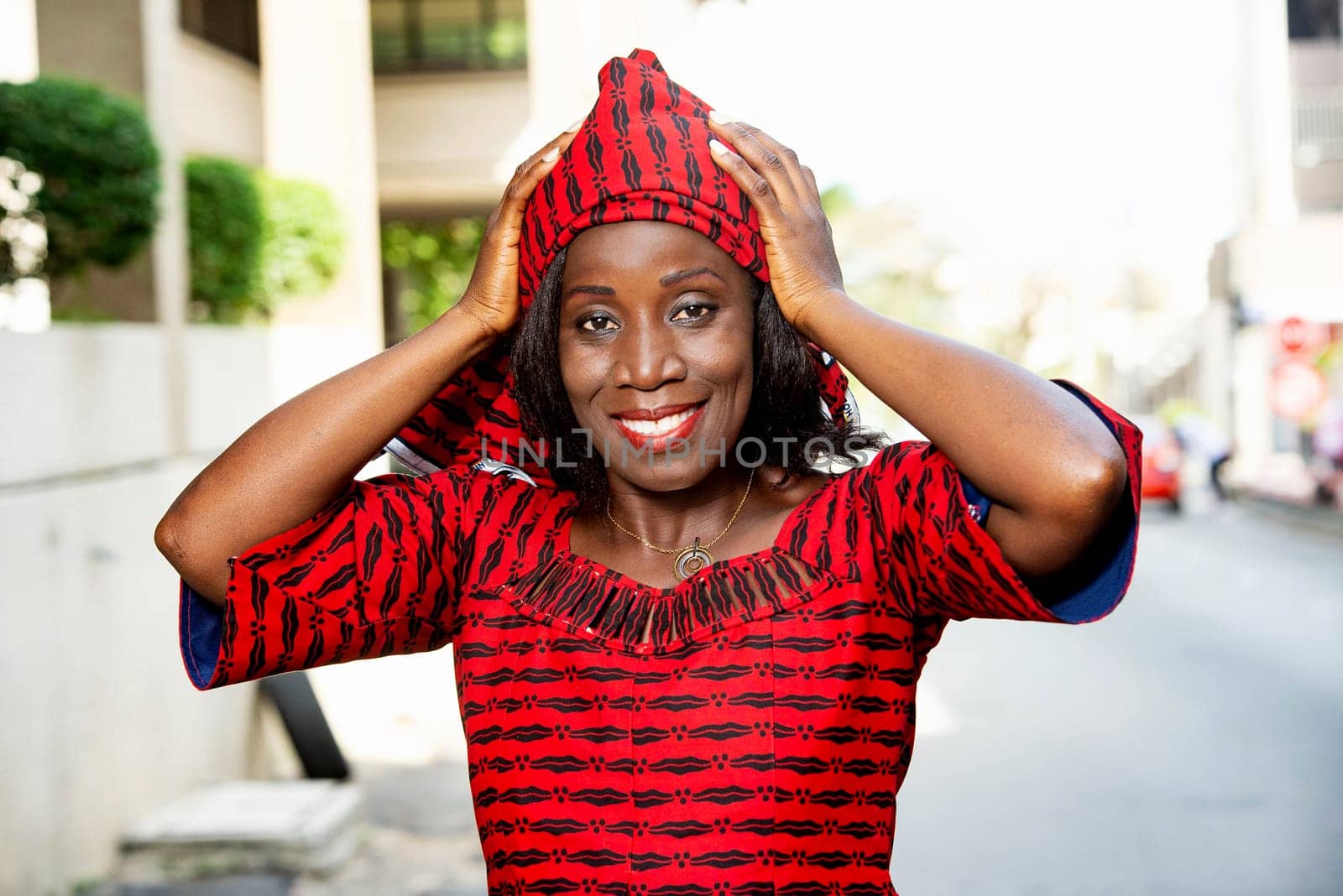 mature african woman standing outdoors adjusting her scarf and looking at the camera smiling.