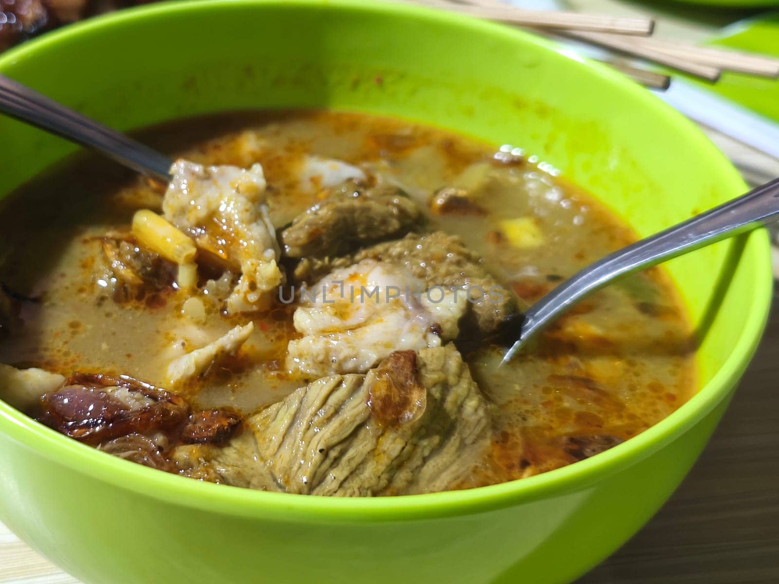A bowl of hearty Gulai Kambing, a rich Indonesian soup brimming with tender goat meat, vegetables, and spices. Served hot on the table.
