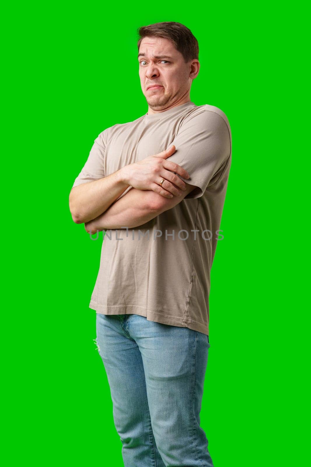 Young man making a disgusted expression while standing against a bright green background in studio