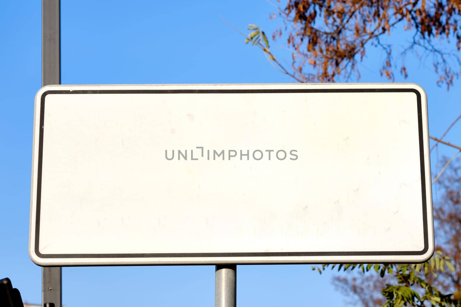 A blank street sign stands alone, surrounded by a peaceful neighborhood. The bright blue sky serves as a backdrop, creating a serene atmosphere.