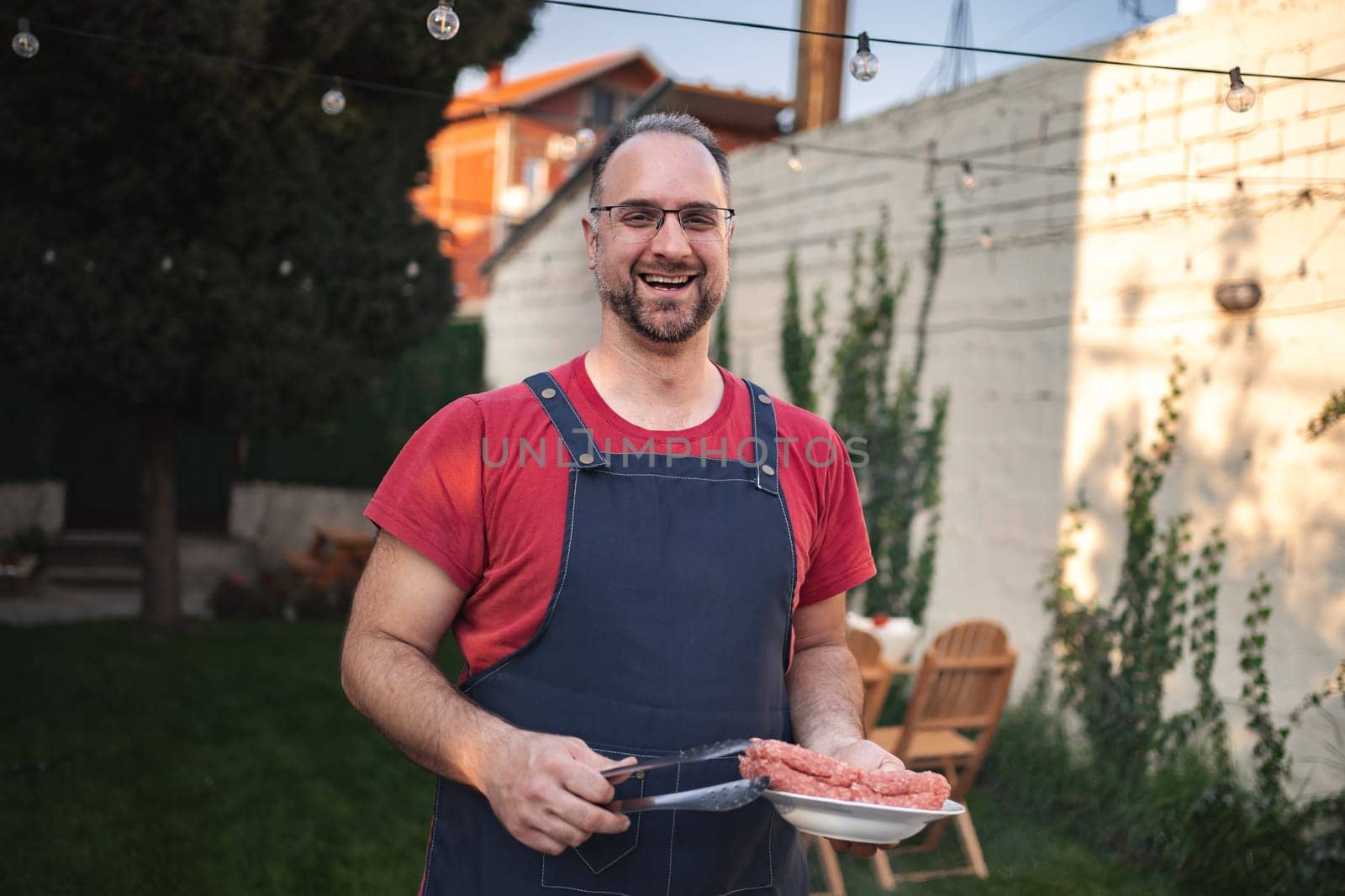 A smiling cook holds ground meat while enjoying the outdoor cooking experience.