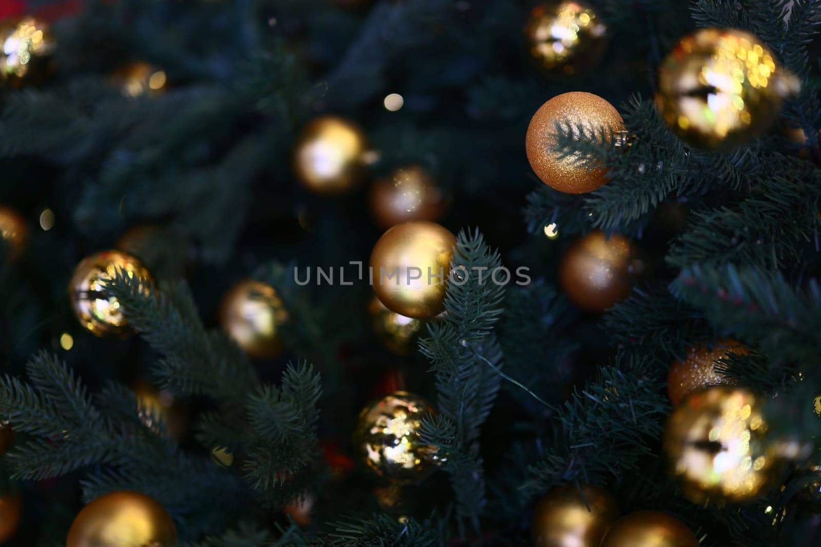 A closeup view of shimmering golden ornaments beautifully adorning a richly green Christmas tree, sparkling