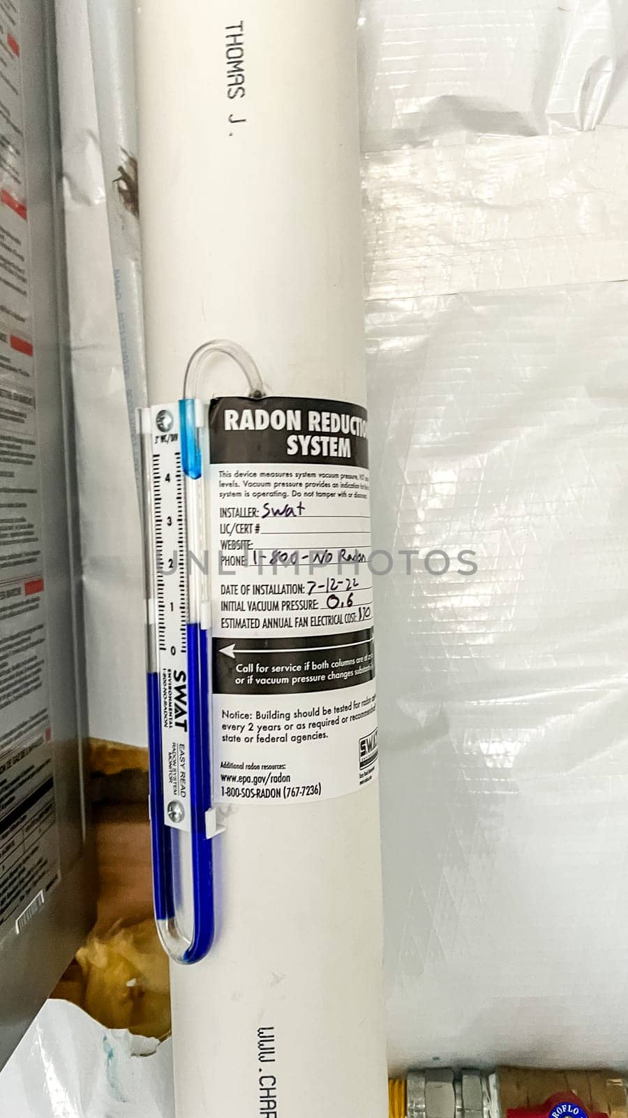 Parker, Colorado, USA-January 11, 2023- A close-up view of a radon reduction system installed in the basement of a newly constructed residential home. The system features a labeled pipe with installation details and a manometer to monitor air pressure, ensuring safe indoor air quality.