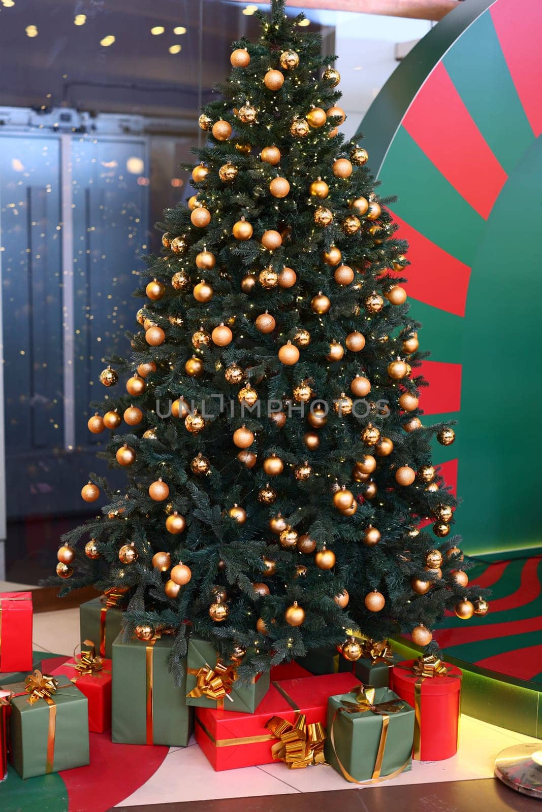 A beautifully decorated Christmas tree adorned with golden ornaments and surrounded by colorful gifts.
