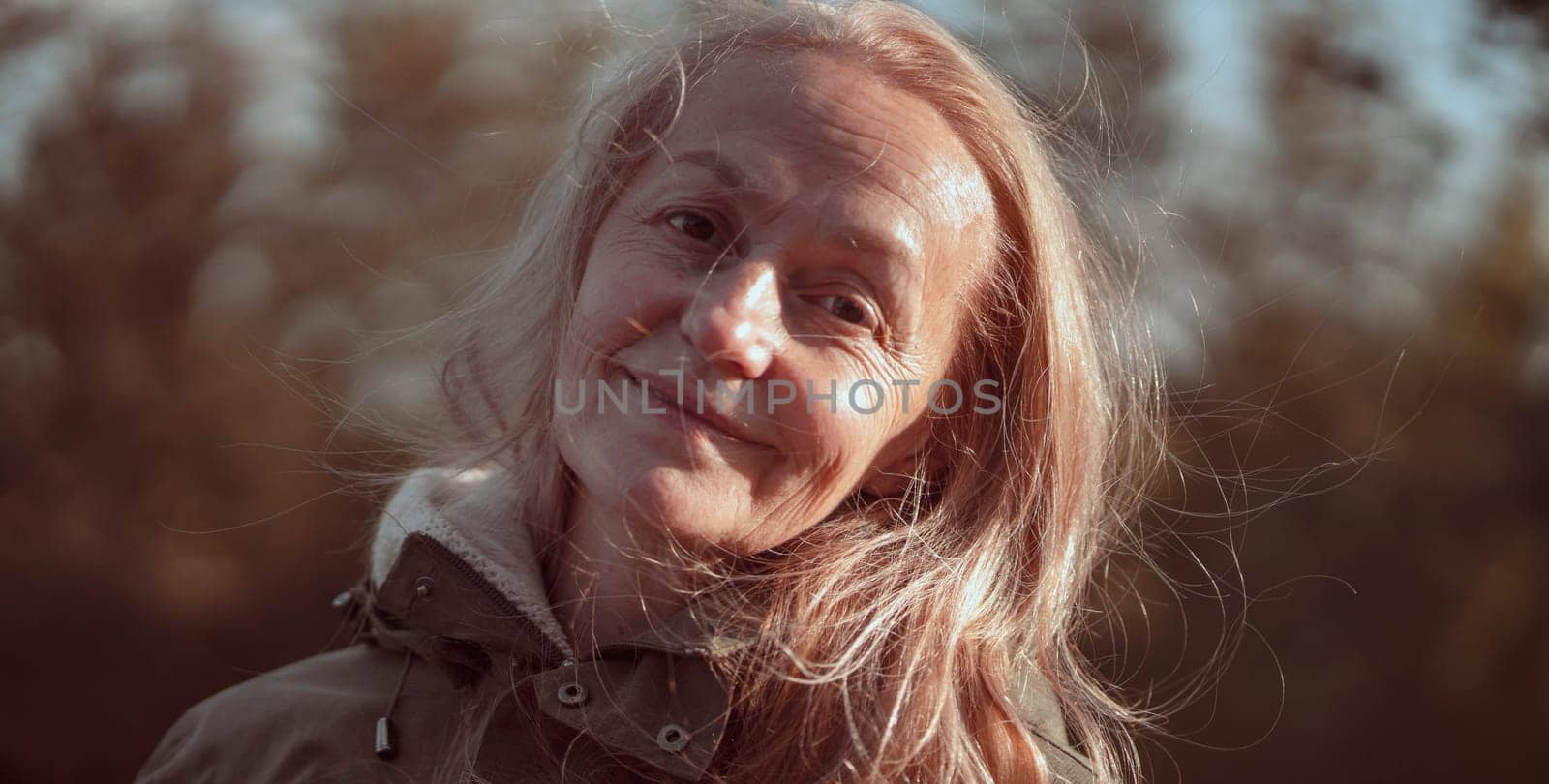 An elderly 60 beautiful woman with a kind smile is walking outdoors on a sunny autumn day, a happy old lady, a grandmother takes care of her appearance, natural beauty with wrinkles portrait closeup.