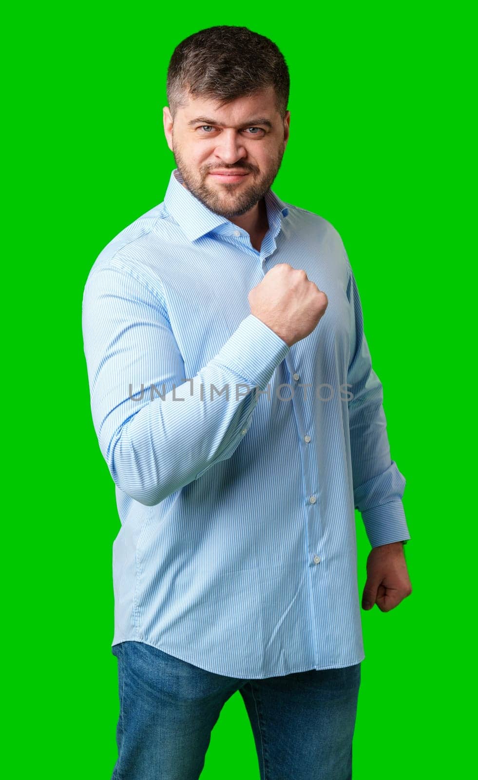 A strong man with fists raised, smiling confidently, on a bright green background in studio