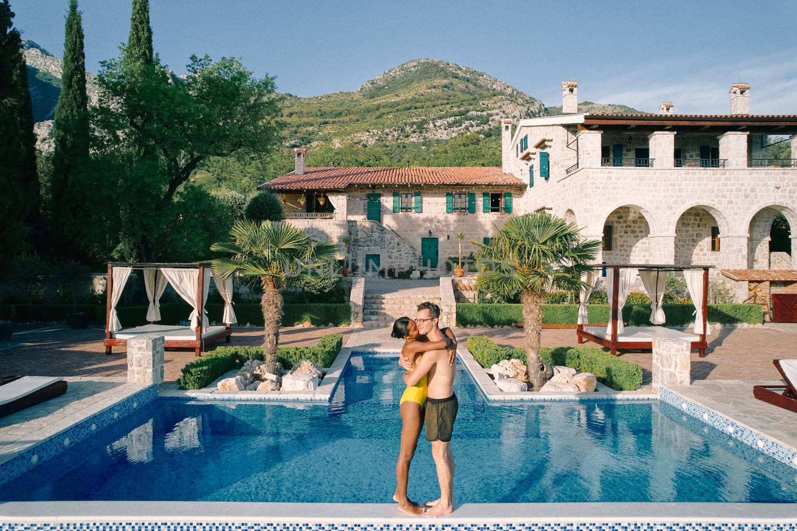 Woman kisses man cheek while hugging him on the edge of a swimming pool in the courtyard of an ancient villa. High quality photo