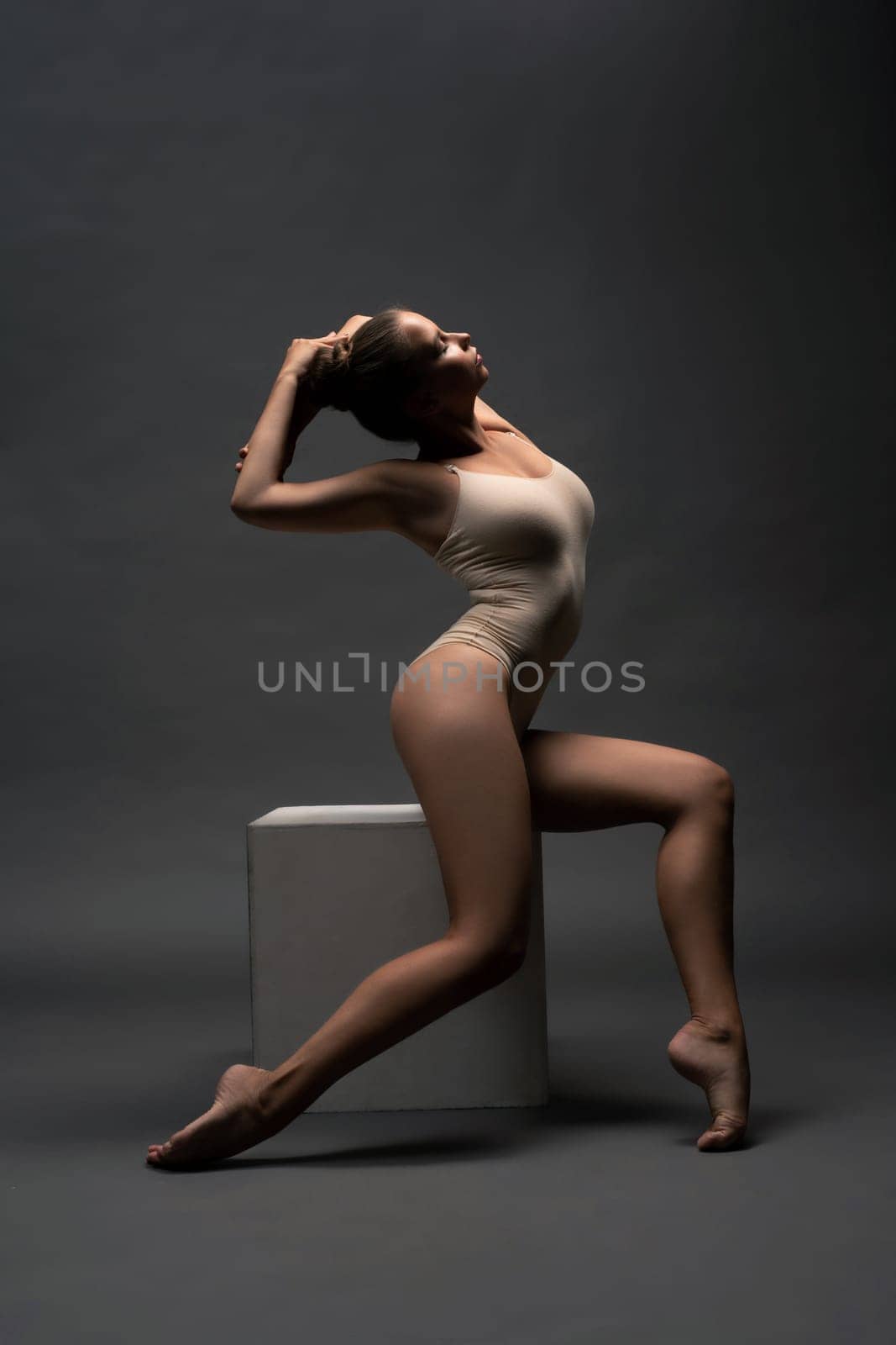 Graceful girl in beige body sitting on the cube profile view