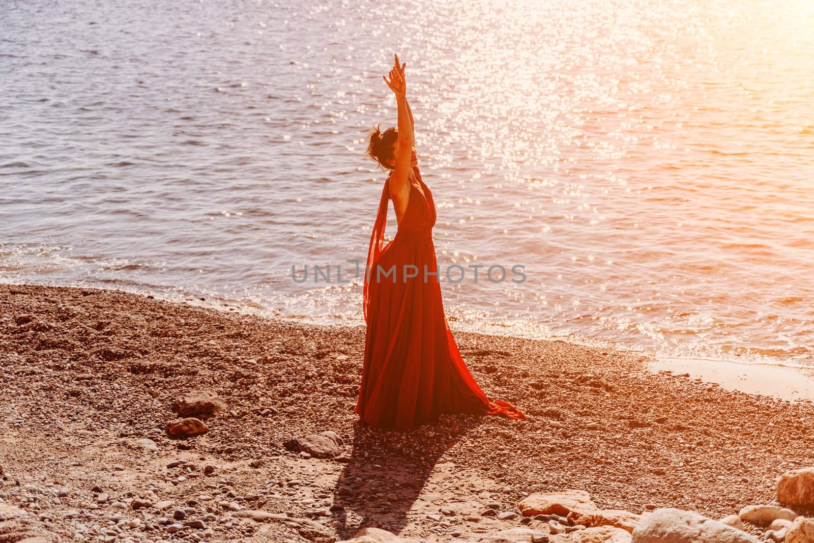 Woman red dress sea. Female dancer in a long red dress posing on a beach with rocks on sunny day. Girl on the nature on blue sky background
