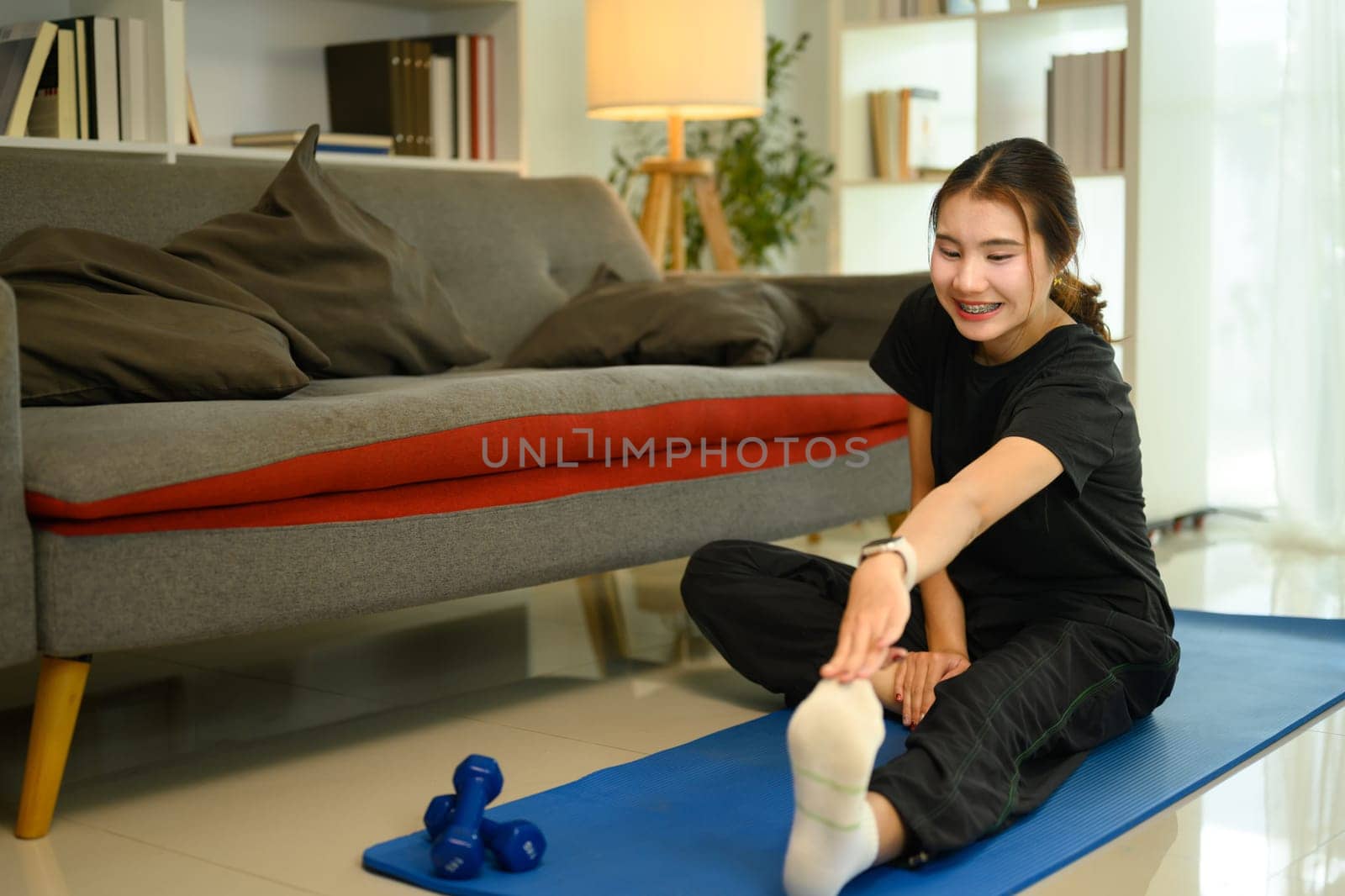 Cheerful asian young woman stretching on a yoga mat in her living room.