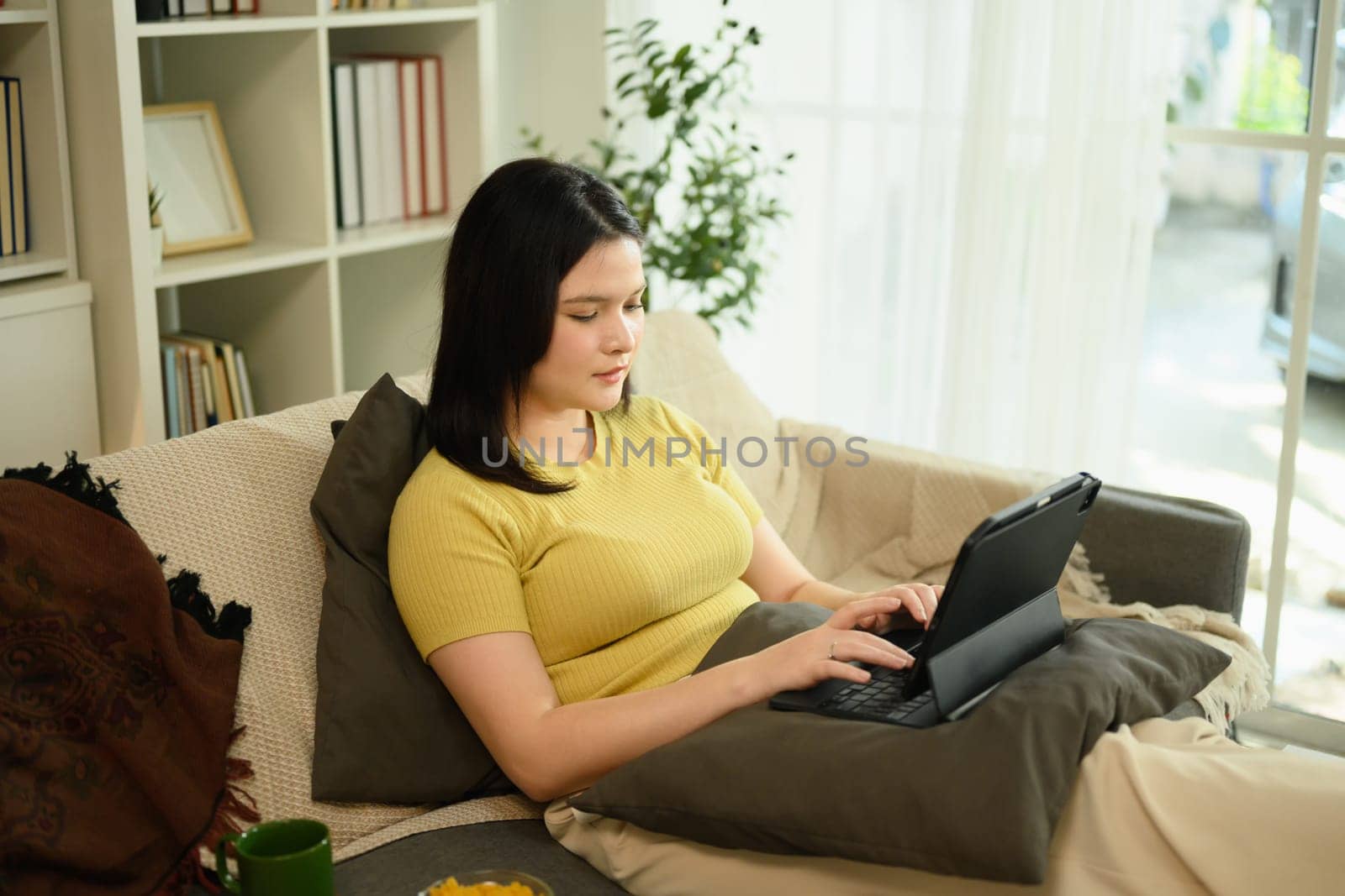Relaxed young woman working with her digital tablet on sofa in bright living room.