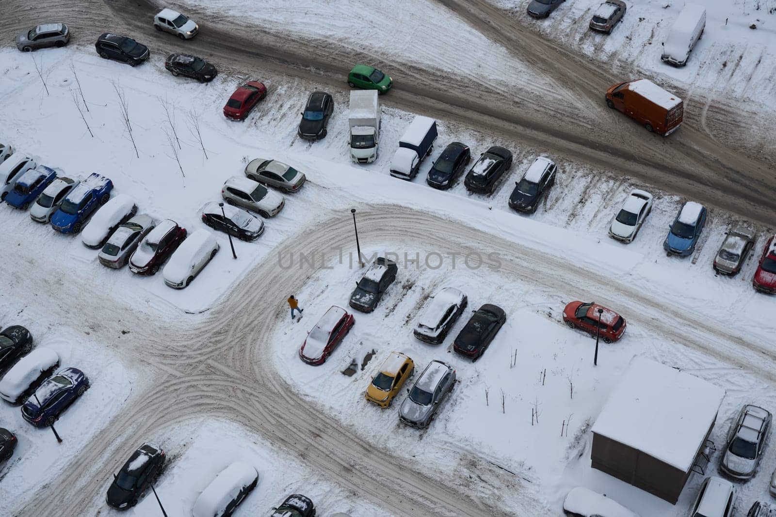 An aerial view of a vast parking lot that is completely blanketed in white snow, showcasing various cars and icy paths