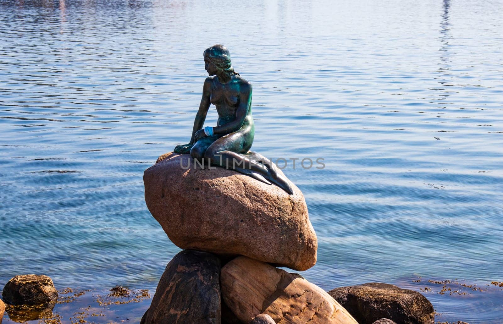 Copenhagen, Denmark - 19 april 2023. The little mermaid sits on the stone with a face mask on her hand. Symbol of Denmark. High quality photo