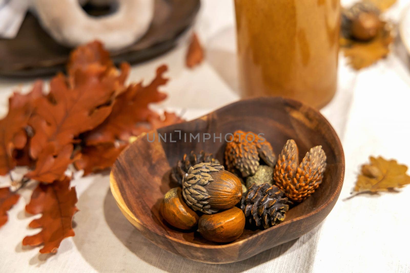 Autumn table decoration with wooden bowl chestnuts, pine cones and oak leaves on table.