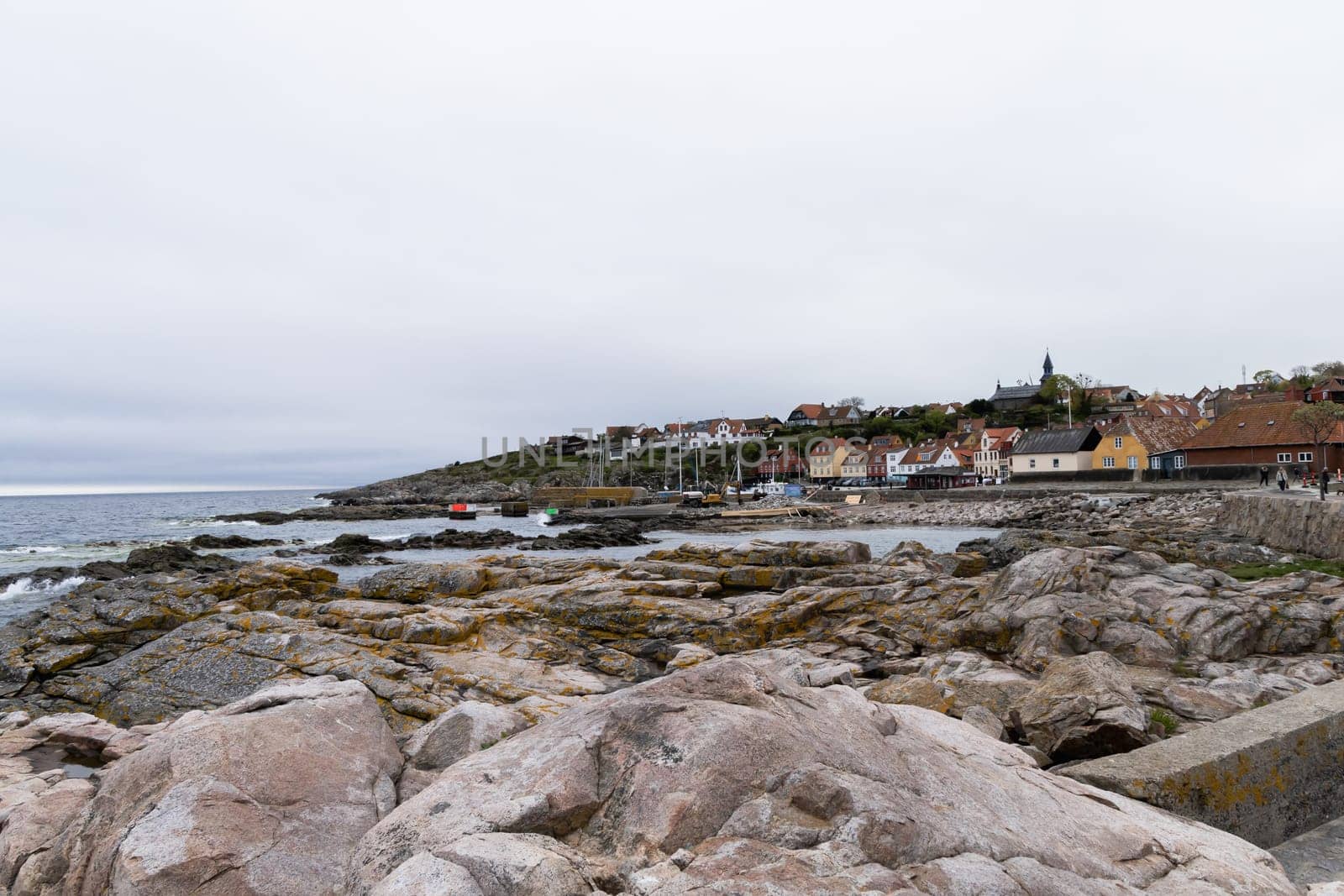 Rocky seashore and a small town in the distance in cloudy weather. Beautiful landscape. Bornholm, Denmark - December 4, 2024