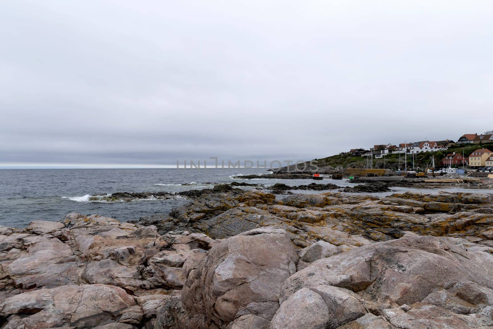 Rocky seashore and a small town in the distance in cloudy weather. Beautiful landscape. Bornholm, Denmark - December 4, 2024