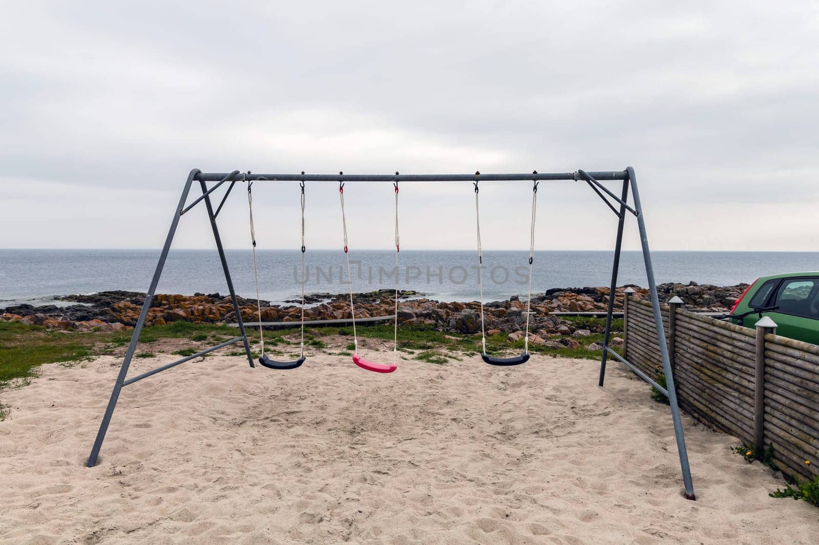 Empty children's swing on the seashore on a cloudy day. High quality photo