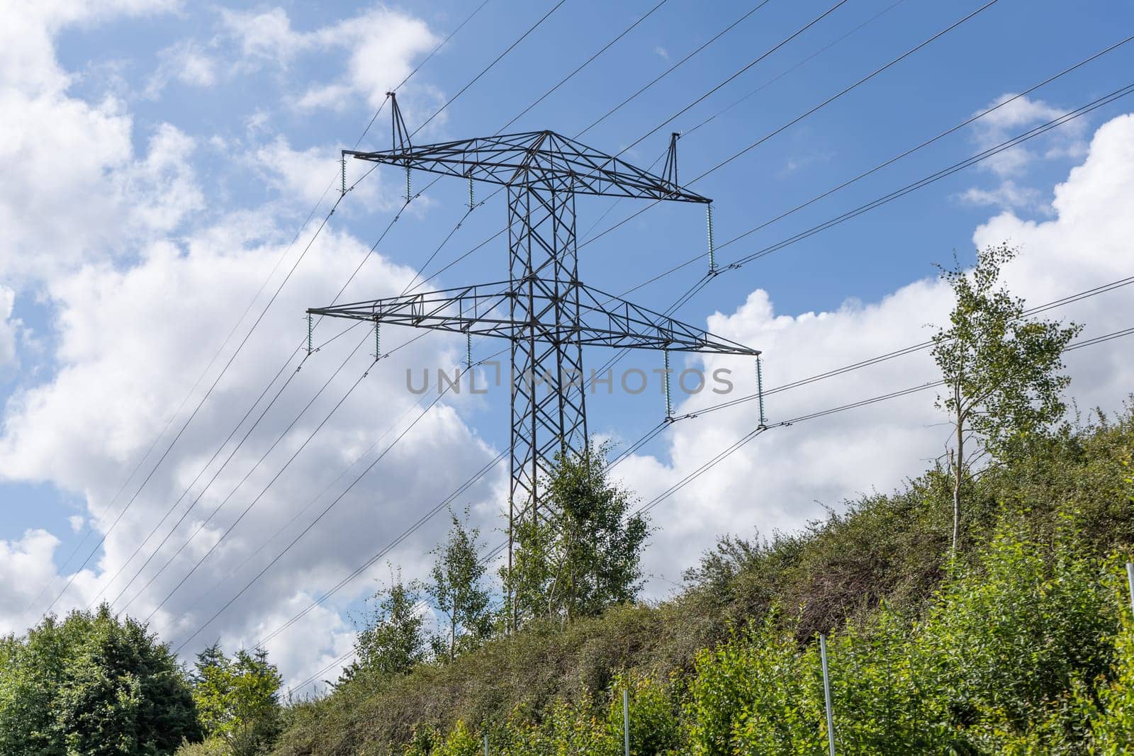 Electricity concept. High voltage power line pylons, electrical tower on a green field with blue sky. High quality photo