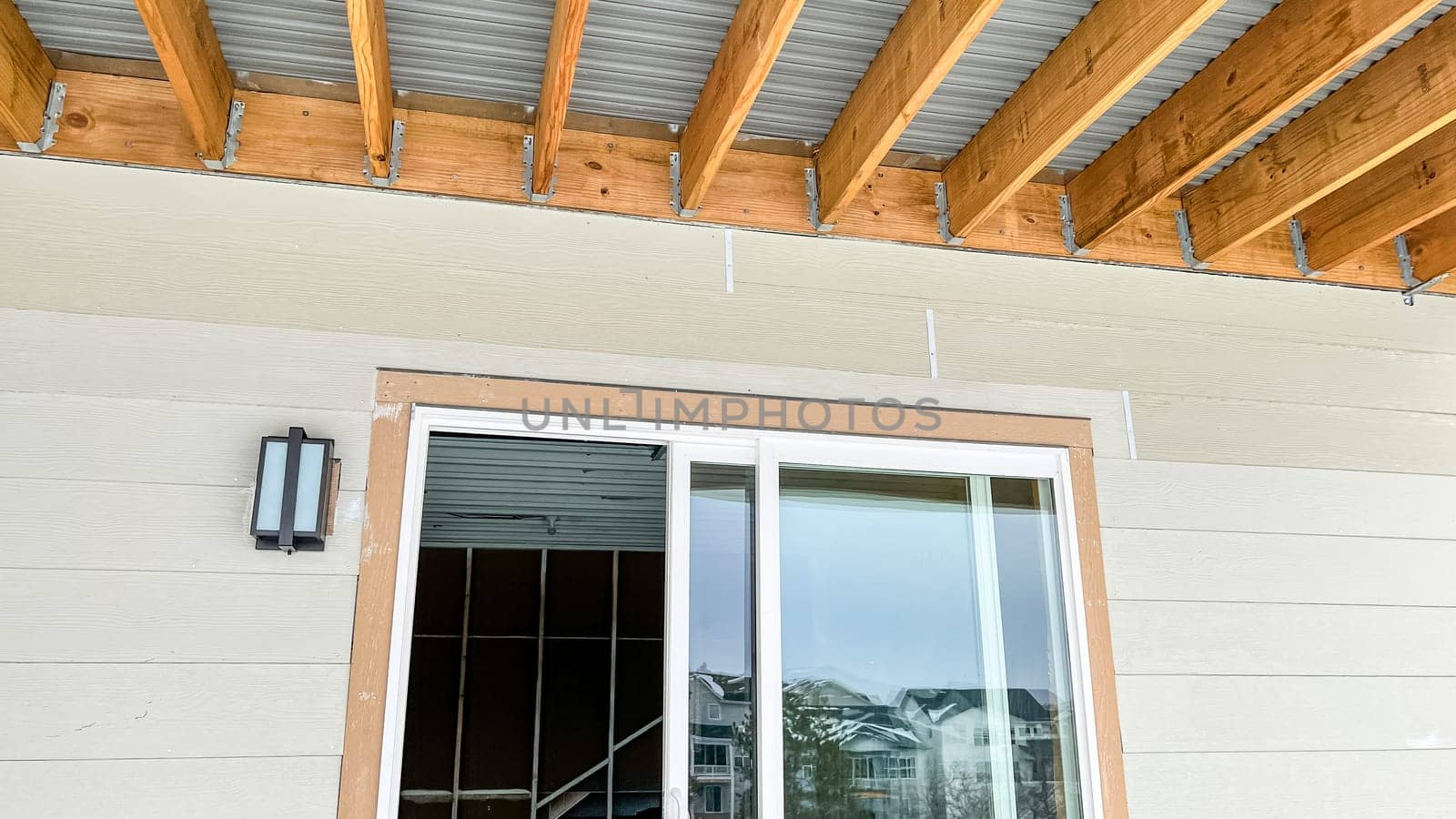 Exposed wood beam ceiling structure supporting a corrugated metal roof in a covered outdoor patio area of a newly built residential home. The design showcases natural wood framing and metal roofing components, providing durability and modern aesthetics.