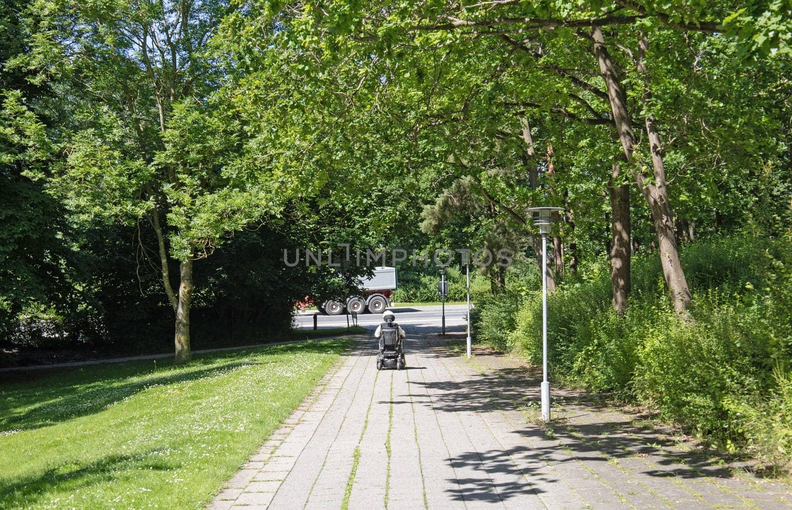 A man in a wheelchair is driving along the road to the parks. High quality photo