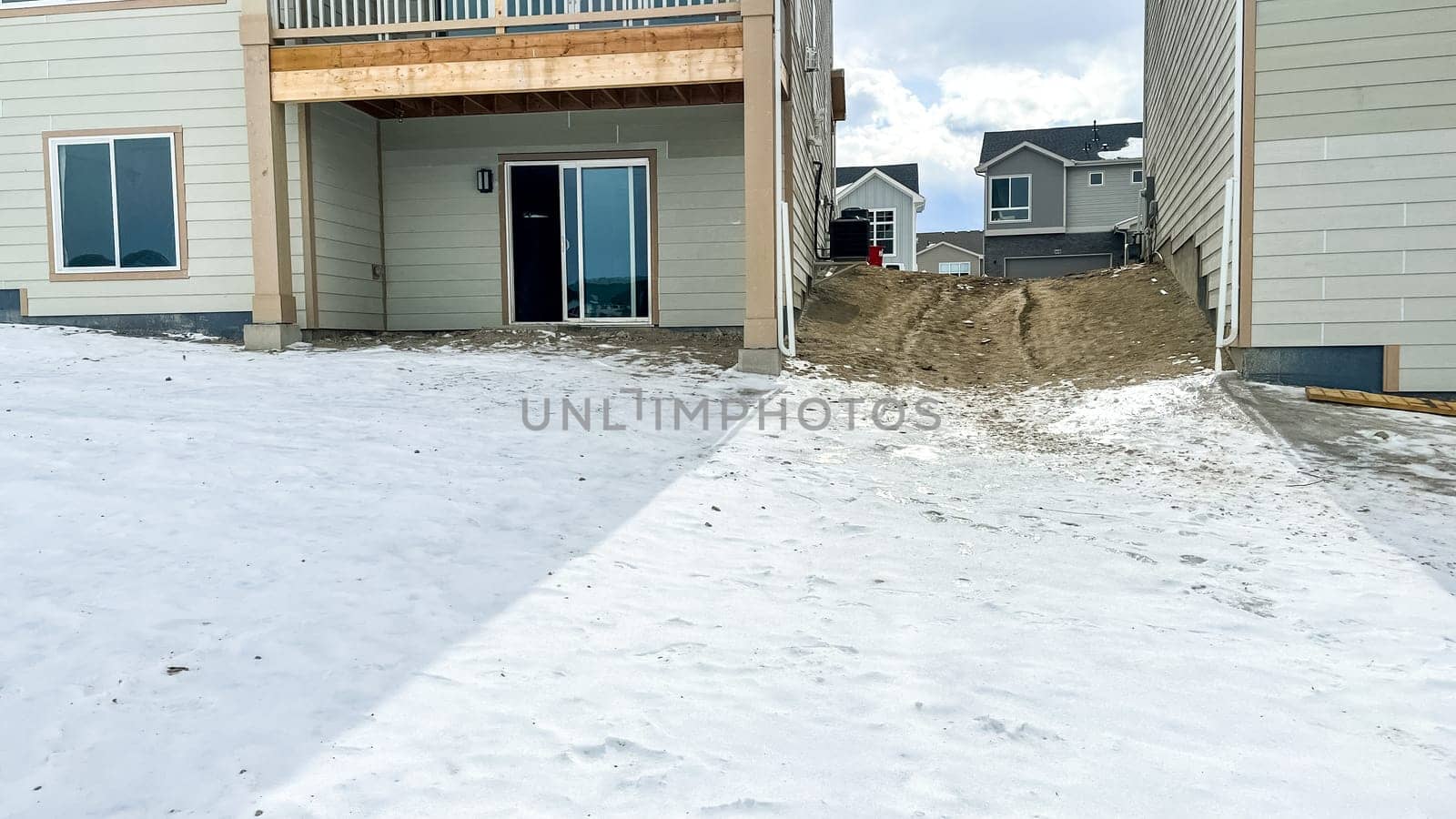Castle Pines, Colorado USA - January 18, 2023-View of the backyard of a newly constructed residential home in a suburban area. Snow covers most of the yard with visible dirt landscaping and unfinished terrain. Sliding glass doors provide access to the basement and an elevated wooden deck adds to the home exterior design.