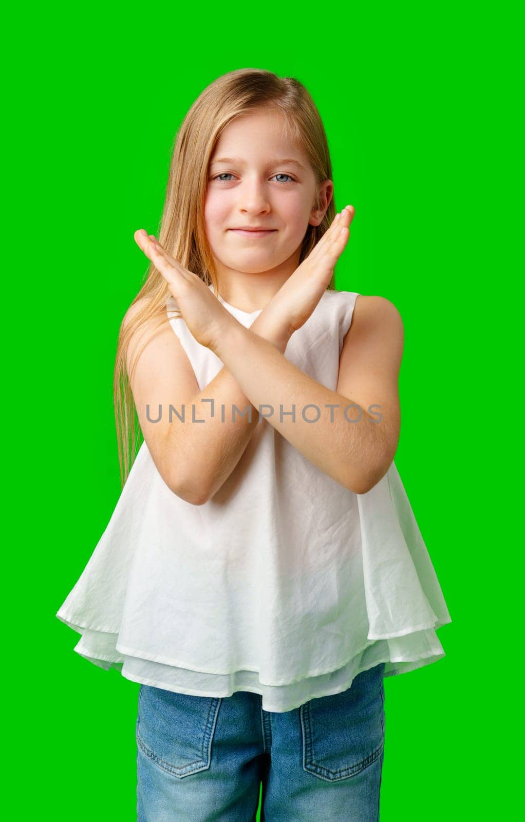 Young girl with long hair making a cross gesture in front of a bright green background in studio