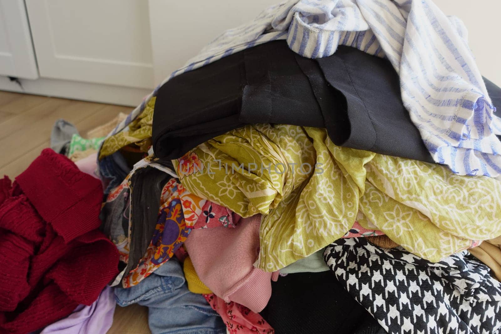 Disorganized clothing pieces are scattered chaotically across a wooden floor surface
