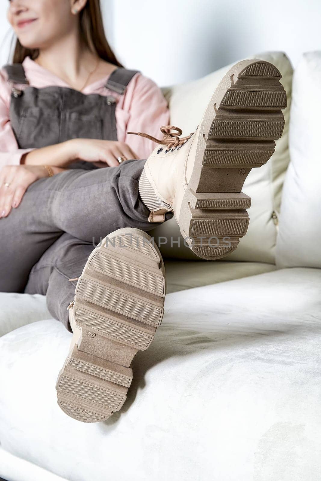 A fashionable model relaxes on a sofa, highlighting trendy shoes that complement her outfit and pose in a cozy setting.