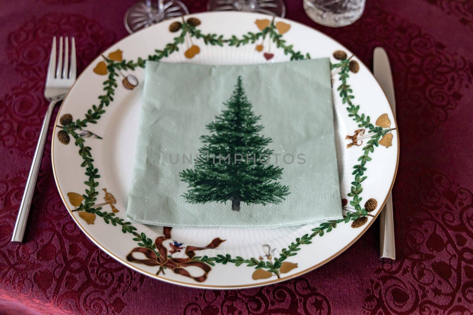 Set Christmas table with Christmas plate and crystal glasses on a red tablecloth.