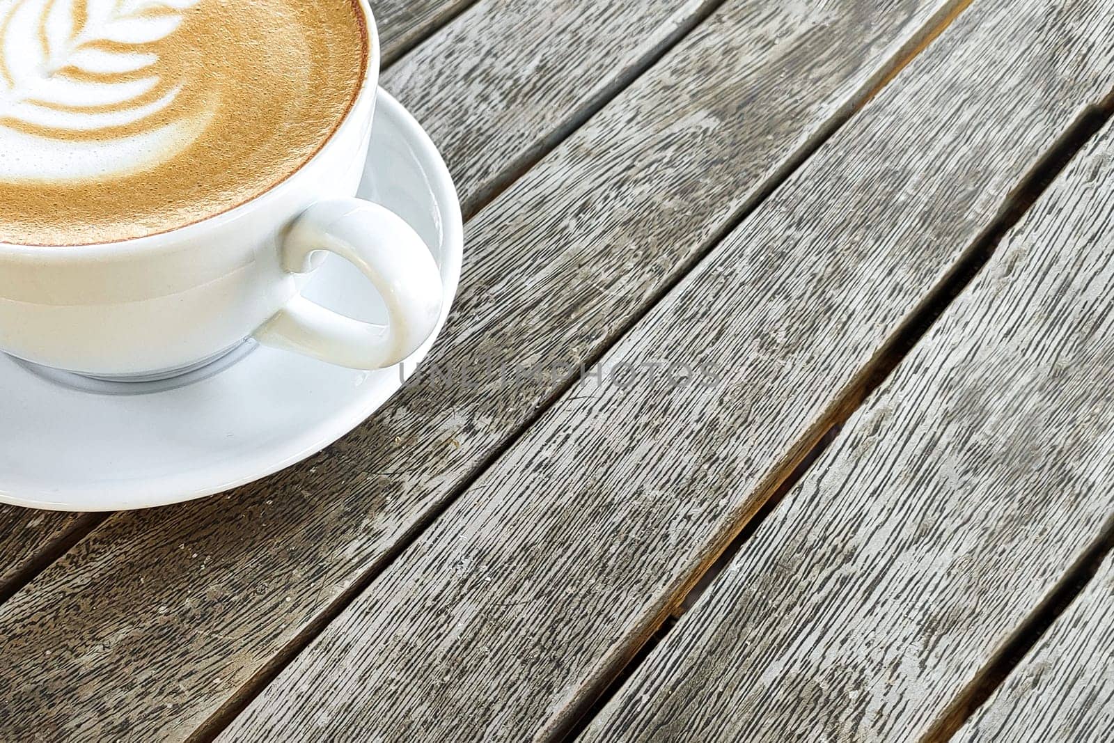 Coffee in white cup with pattern on top of foam, against background of wooden table, copy space. by Laguna781