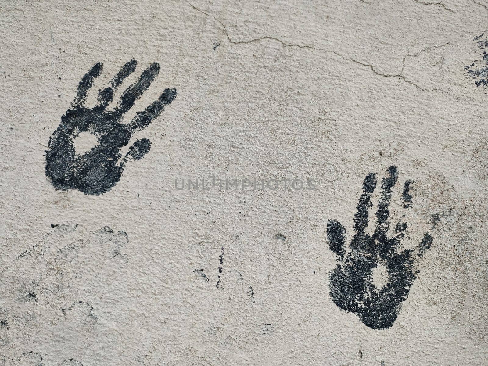 Pair of black prints of children's palms diagonal arrangement on gray concrete wall, copy space by Laguna781