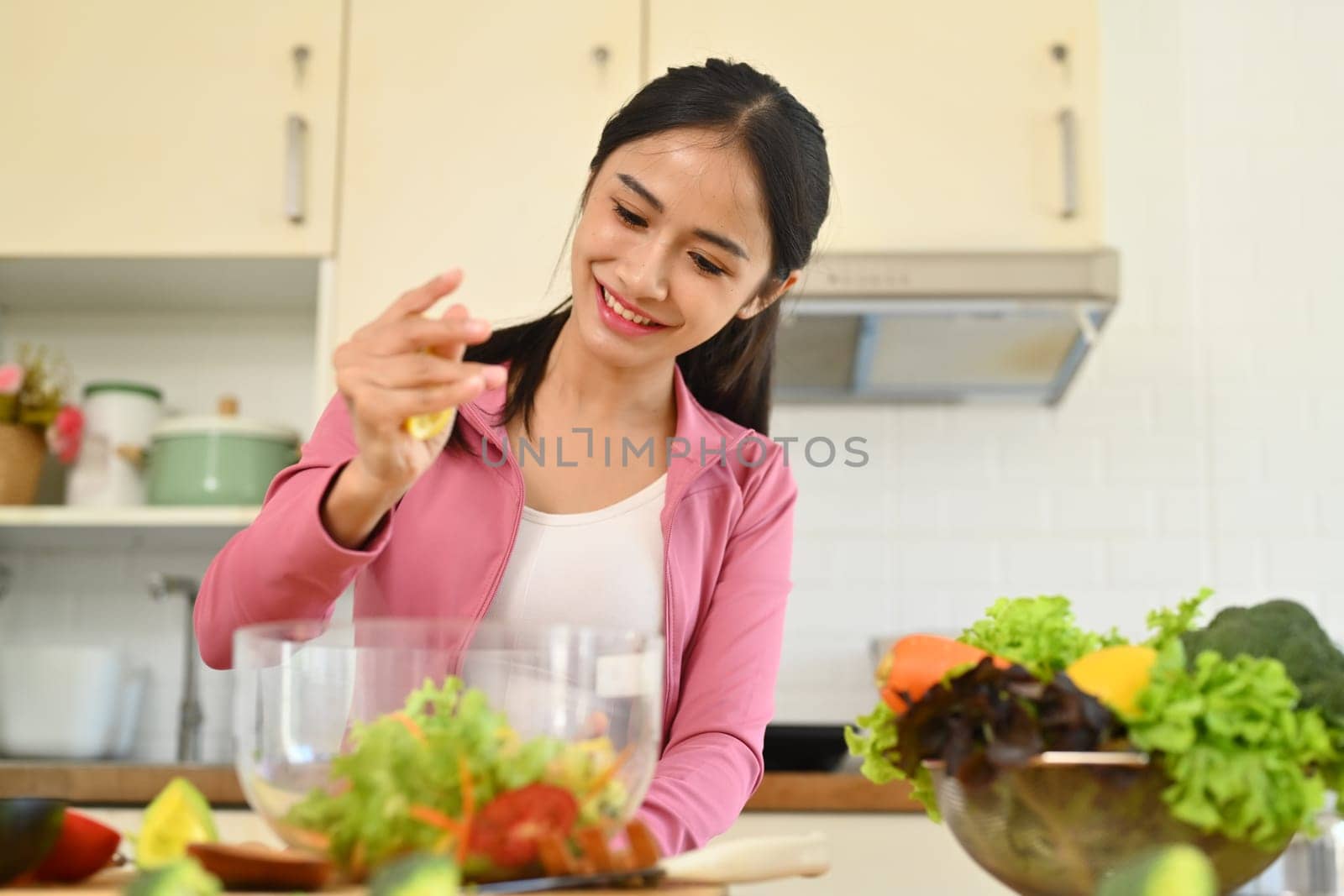 Happy young woman squeezing fresh lemon juice into bowl with vegetable salad. Healthy eating concept by prathanchorruangsak