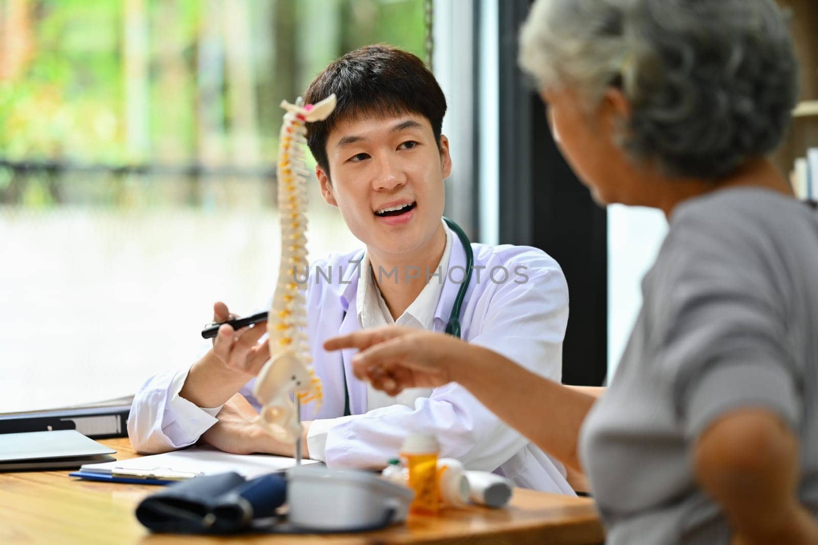 Male orthopedist explaining structure of spine to mature female patient in clinic. Health care concept by prathanchorruangsak