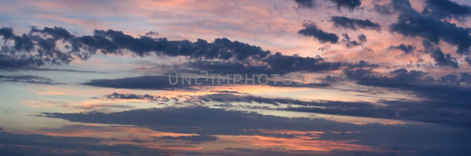 Panoramic view of the vast sky, dominated by a variety of clouds, hints of pink and blue suggest the interplay of the setting or rising sun, creating a soothing, calm atmosphere