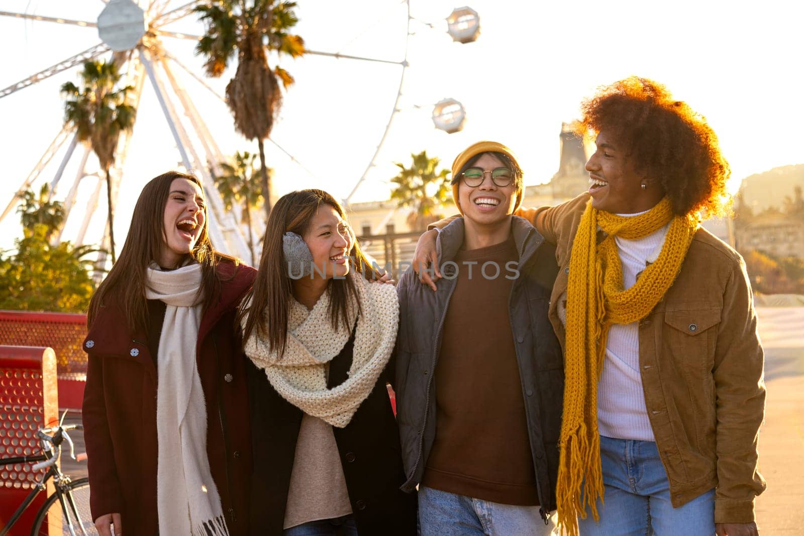 Group of happy multiracial college student friends laughing embracing together while walking around city on a sunny winter day. Friendship and lifestyle concept.