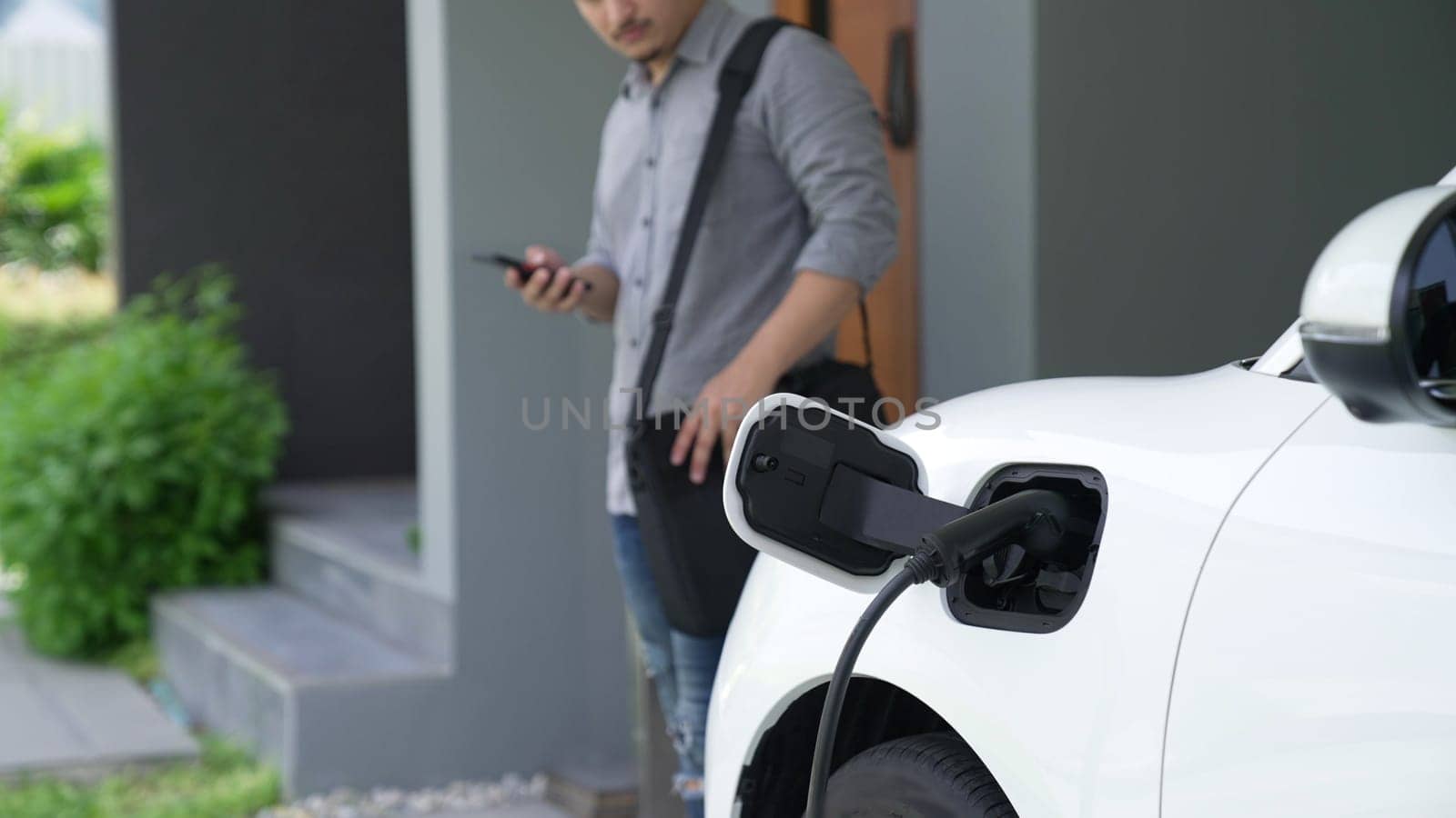 A man unplugs the electric vehicle's charger at his residence. Concept of the use of electric vehicles in a progressive lifestyle contributes to a clean and healthy environment.