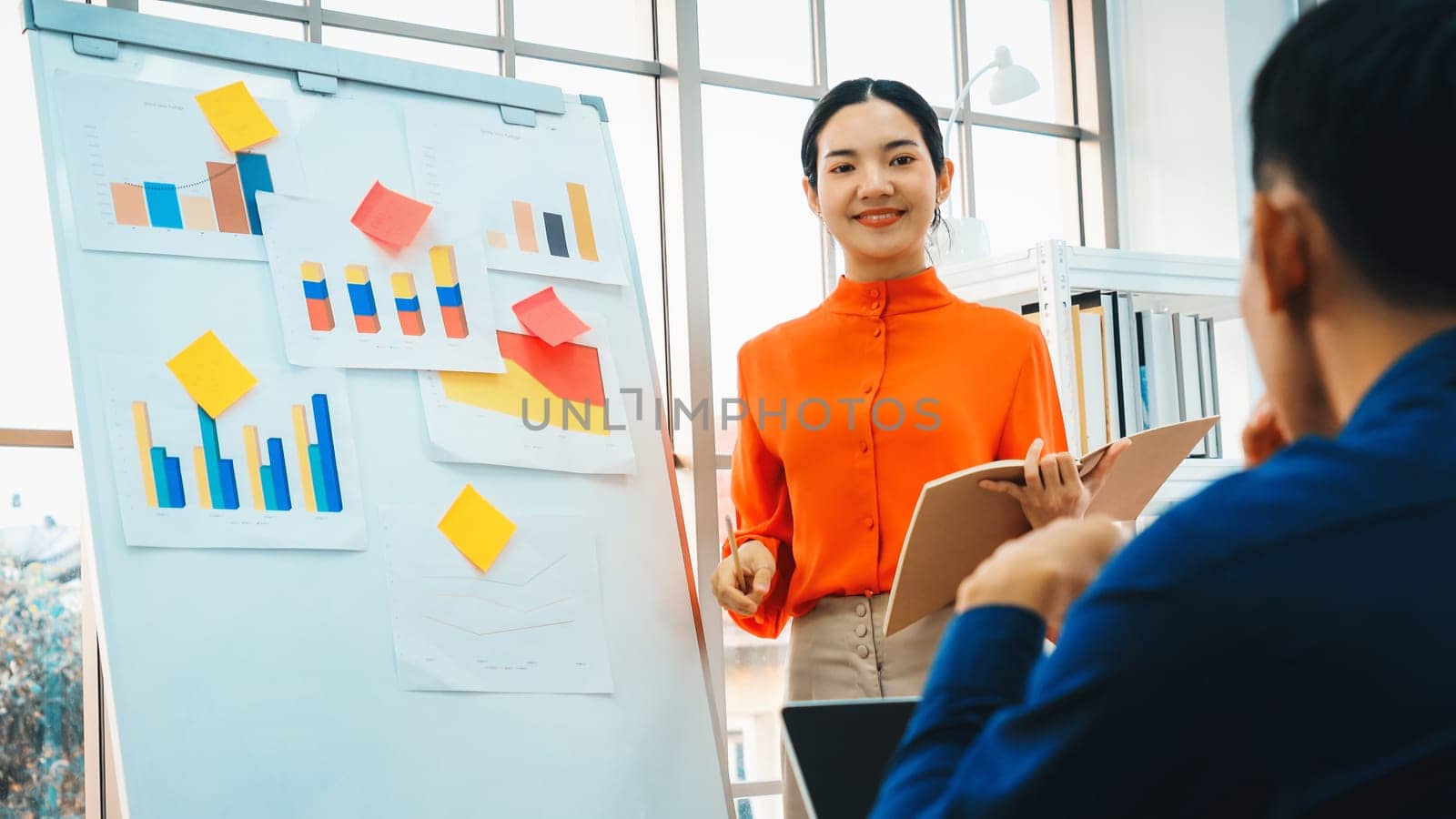 Young woman explains business data on white board in casual office room . The confident Asian businesswoman reports information progress of a business project to partner to determine strategy . Jivy