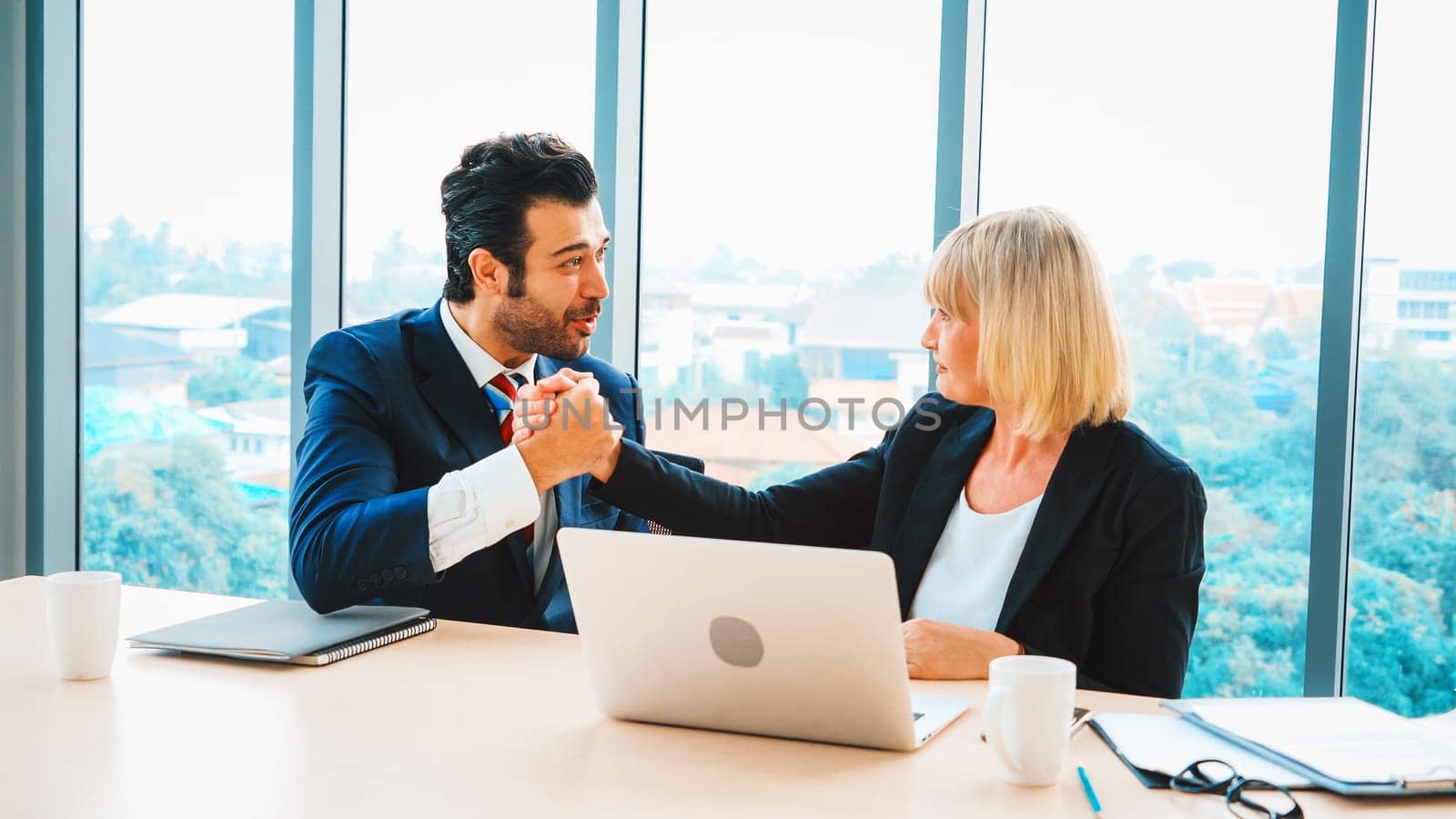 Two happy business people celebrate at office meeting room. Successful businessman congratulate project success with colleague at modern workplace while having conversation on financial report. Jivy