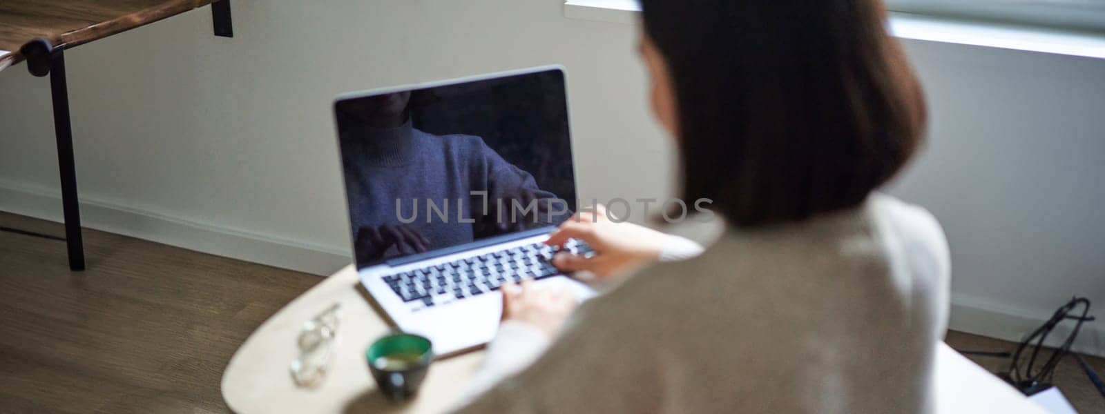 Rear view of woman, typing and working on laptop, computer screen is empty for copy space, female student studying remotely.