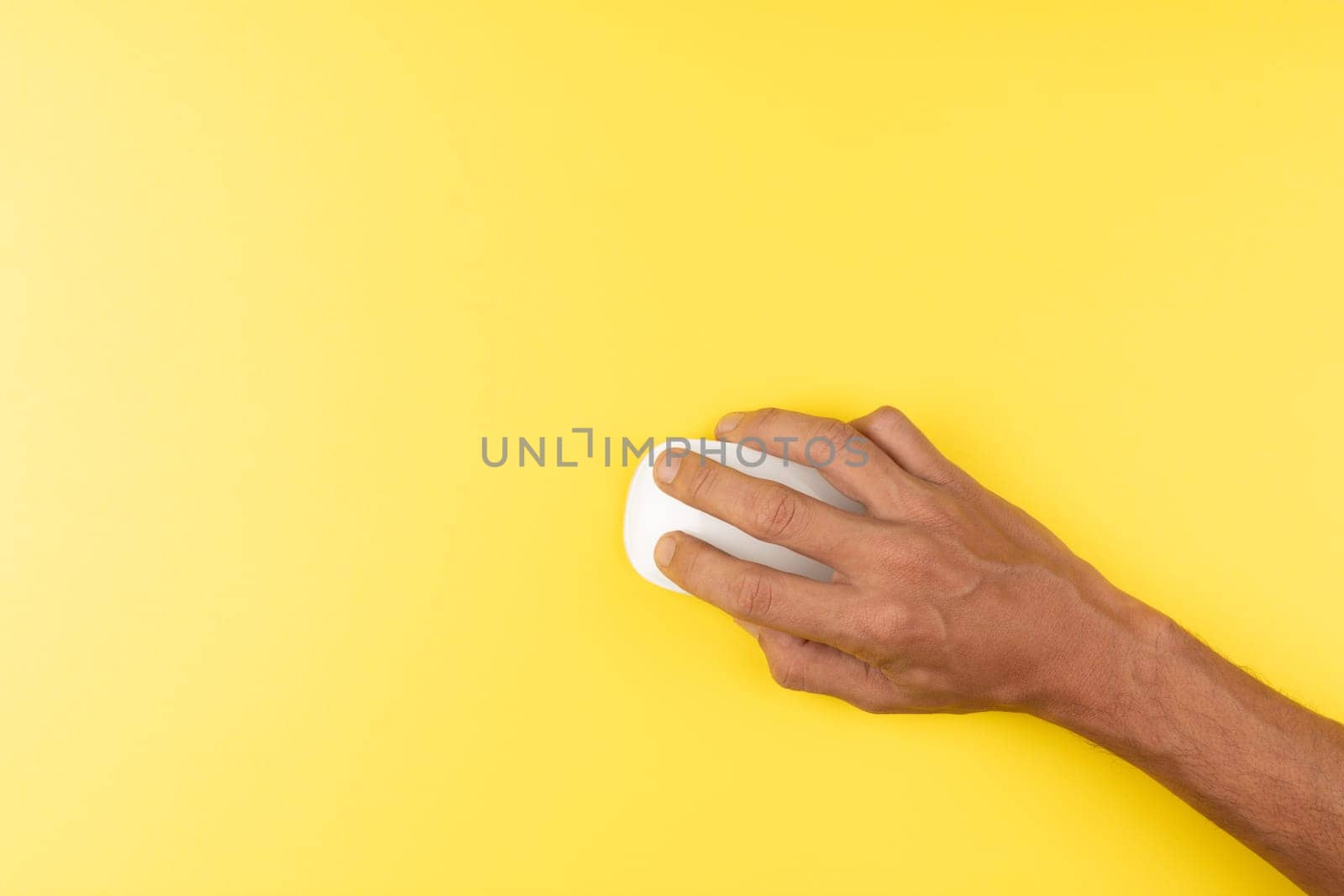 First person top view photo of black male hand with white computer wireless mouse on isolated yellow background with copyspace