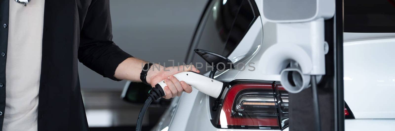 Young man travel with EV electric car to shopping center parking lot charging in downtown city showing urban sustainability lifestyle by green clean rechargeable energy of electric vehicle innards