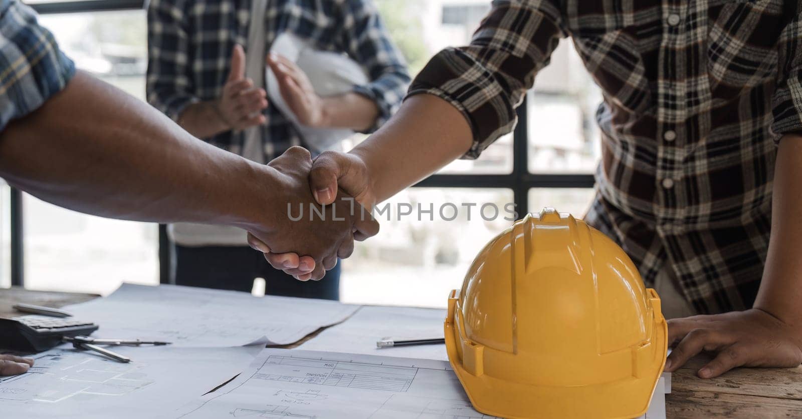 A team of engineers who successfully planned work on a modern home construction project shook hands and congratulated the team on their success. by wichayada