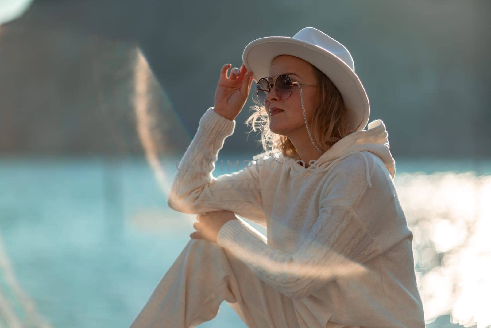 Happy blonde woman in a white suit and hat posing at the camera against the backdrop of the sea.