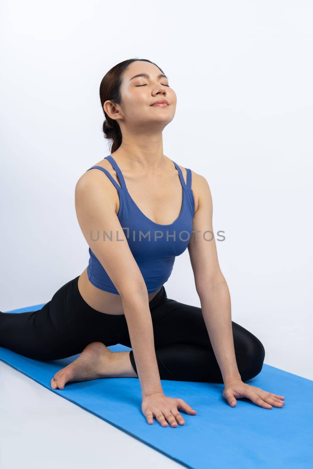 Asian woman in sportswear doing yoga exercise on fitness mat as her workout training routine. Healthy body care and calm meditation in yoga lifestyle in full body shot on isolated background. Vigorous