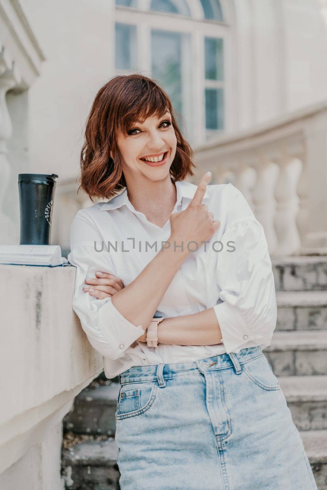 Woman building city. A business woman in a white shirt and denim skirt stands leaning against the wall on the steps of an ancient building in the city.
