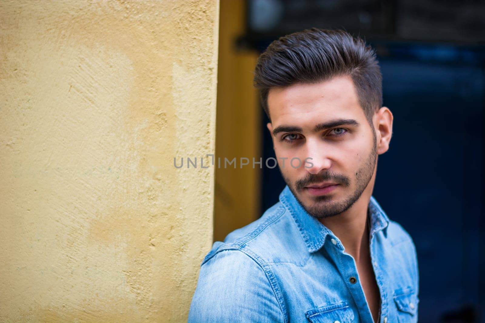 A man in a denim shirt leaning against a wall