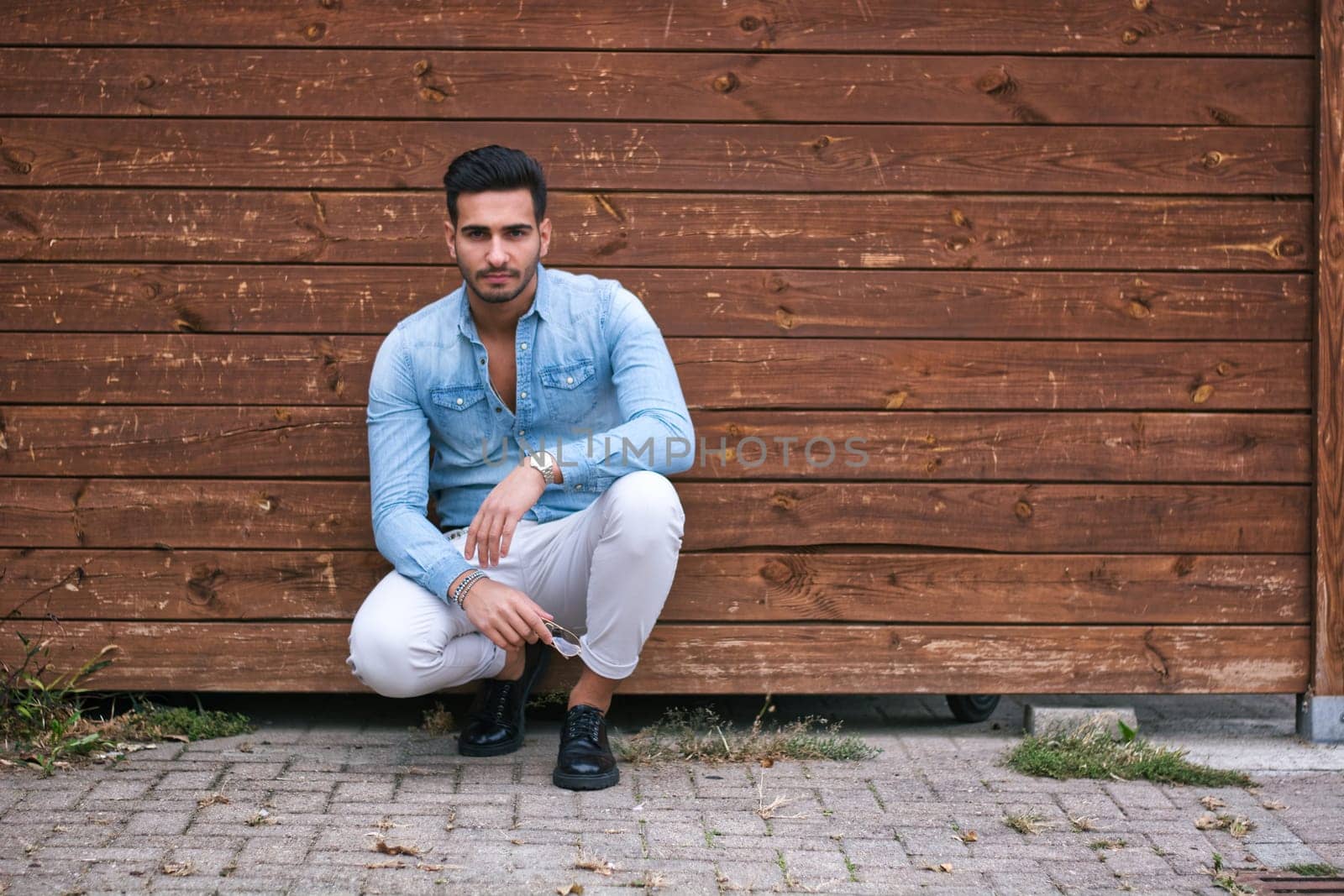 A man sitting on the ground in front of a wooden wall