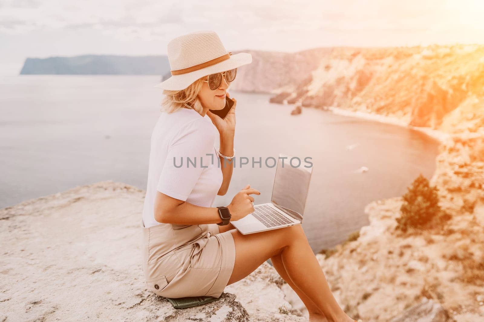 Digital nomad, Business woman working on laptop by the sea. Pretty lady typing on computer by the sea at sunset, makes a business transaction online from a distance. Freelance, remote work on vacation by panophotograph