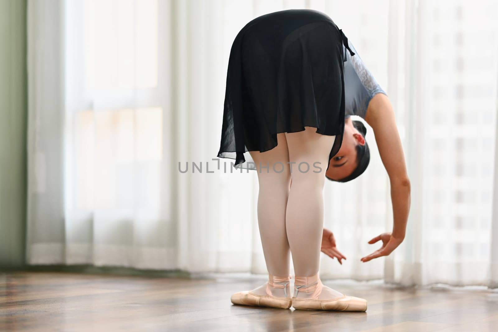 Young ballerina practice ballet near window in dance class. Dance, art, education and flexibility concept.